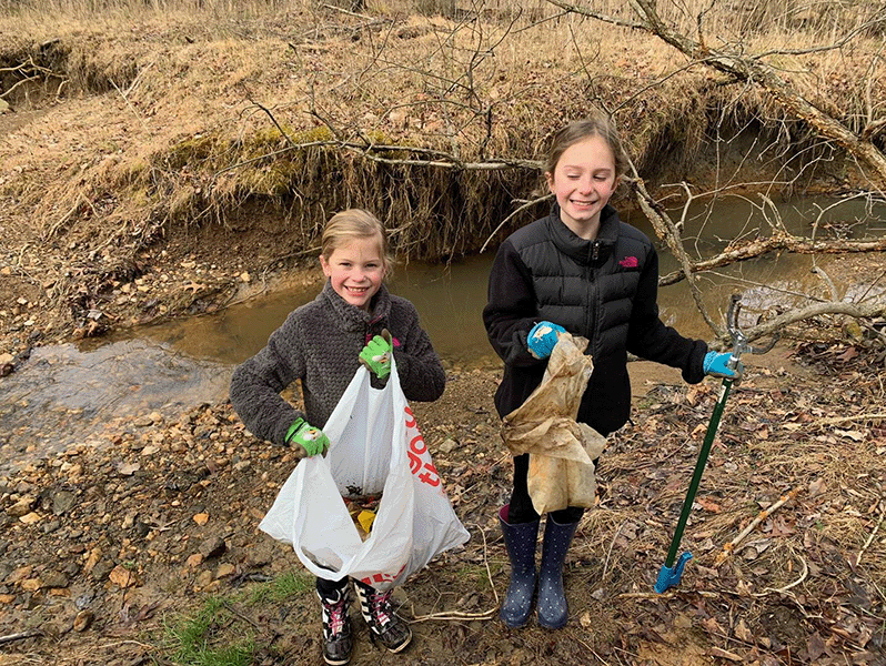 Two young students holding trash bag and plogging stick