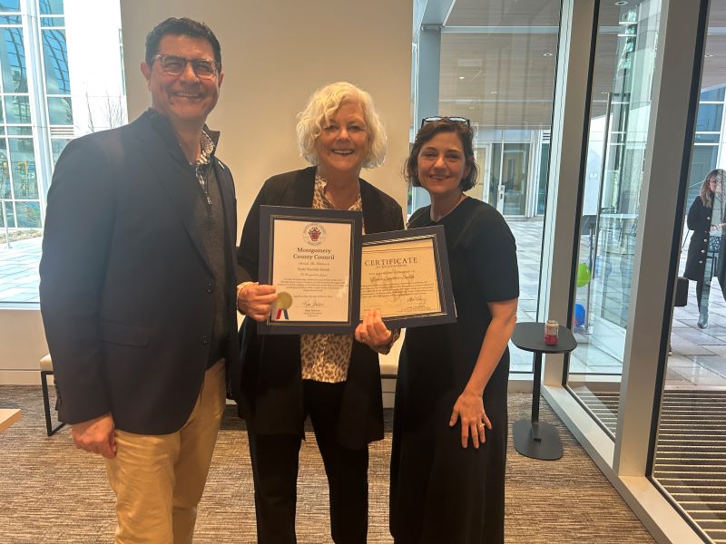 Miembro del Concejo Gabe Albornoz, Sra. Sinclair-Smith y la presidenta del Concejo Kate sonríen para una foto mostrando una proclamación y certificado del Concejo.