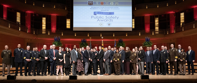 A group of uniformed public safety leaders and public officials stand on Strathmore stage. A large banner reads “51st Annual Public Safety Awards”.