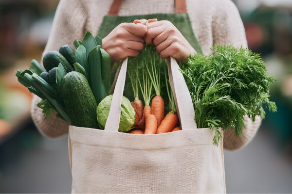 Grocery shopper holding canvas bag filled with produce.