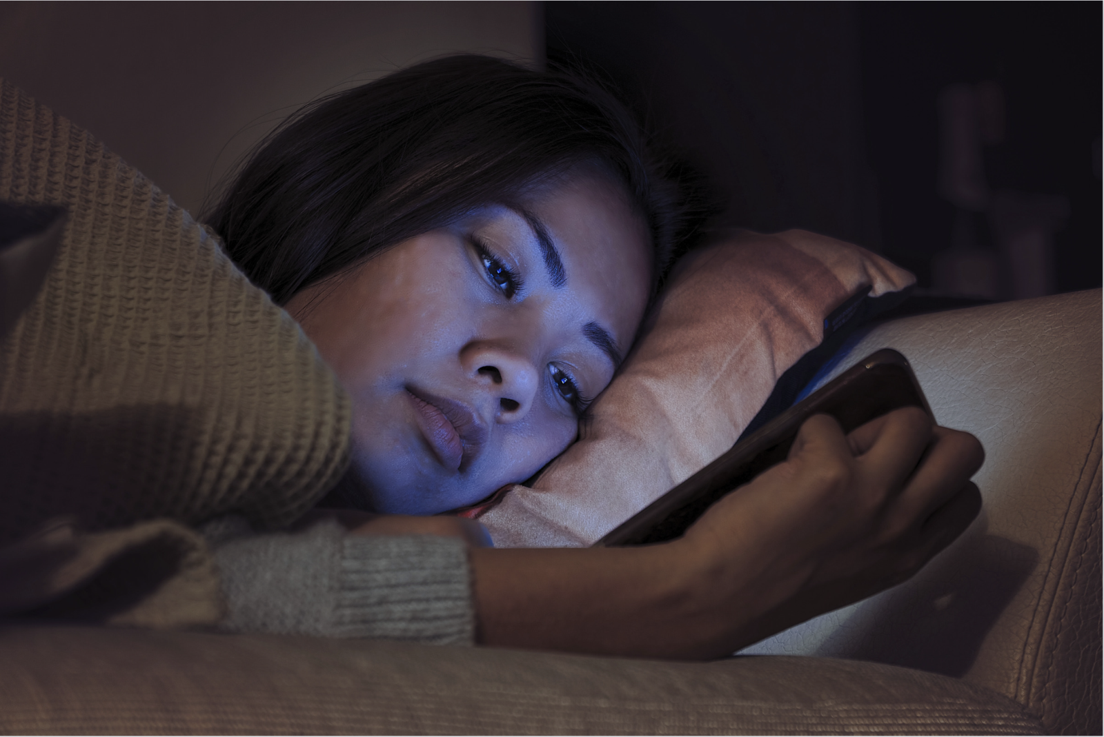 Sad woman looking at phone in bed