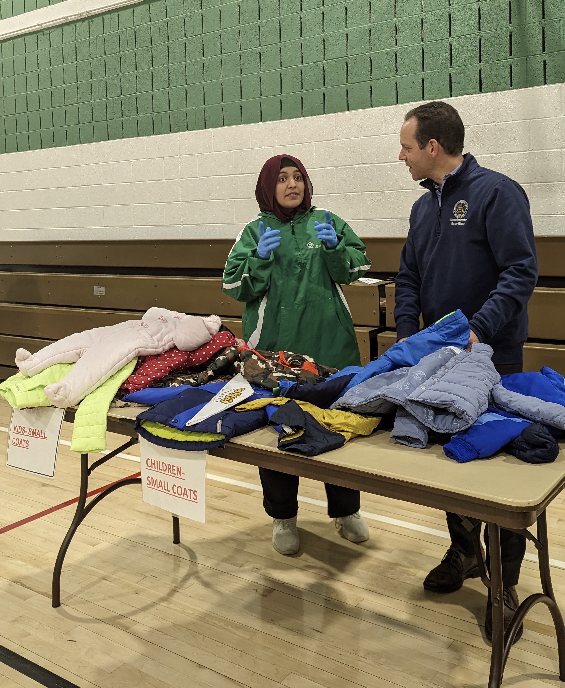 Presidente del Concejo Glass distribuye abrigos con un voluntario en el gimnasio dentro del centro de recreación de Long Branch.