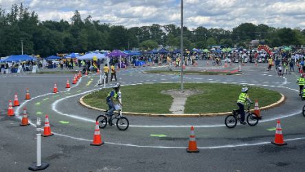 Kids ride on bikes around a flag pole in parking lot