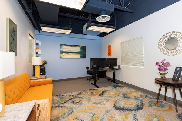 colorful office, with yellow sofa, patterned carpet, round mirror and light blue accent wall
