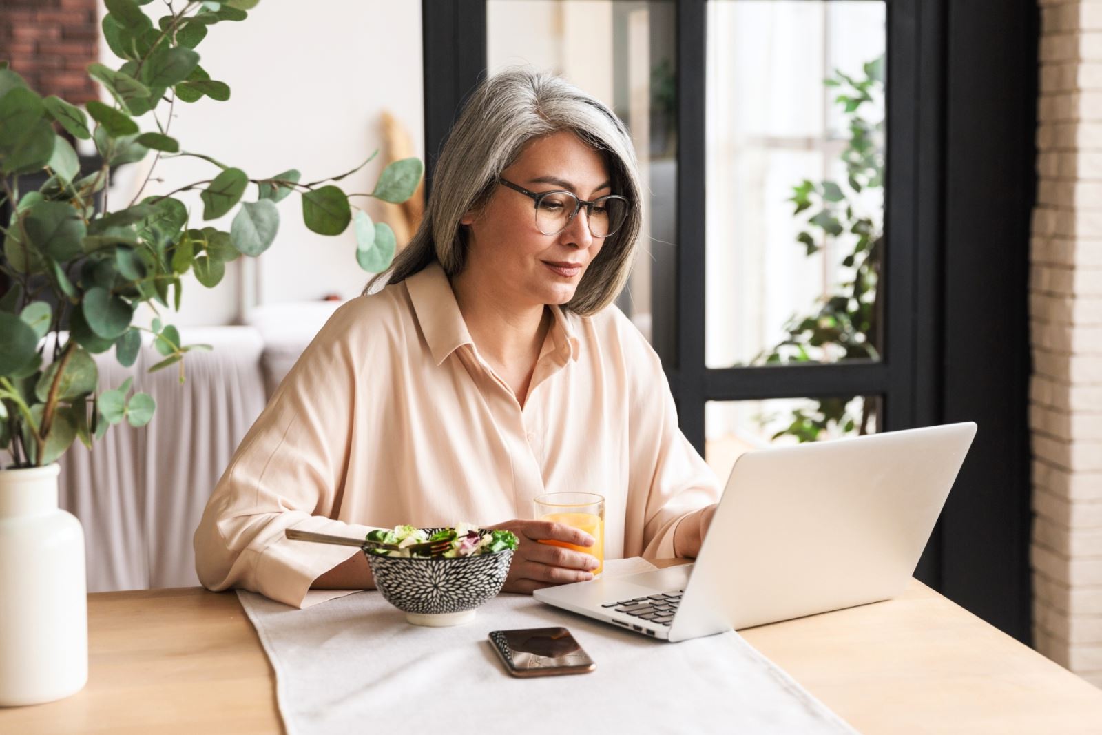 senior woman typing on laptop at dining table