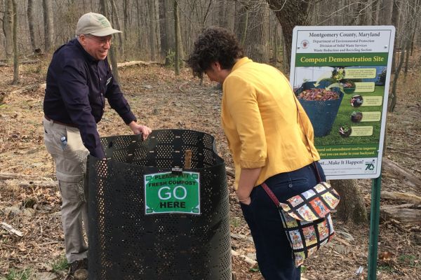 Two people at backyard composting demonstration using a black mesh compost bin.