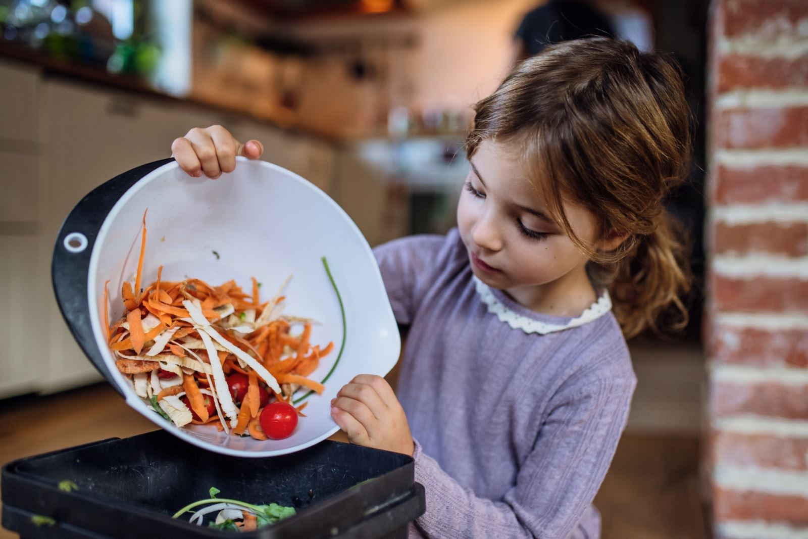 girl adding food scraps to kitchen compost container