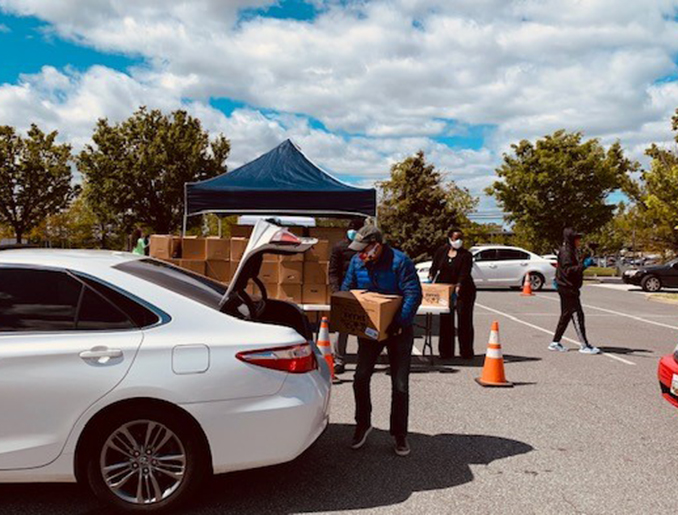 Person carrying food box to car with open trunk.