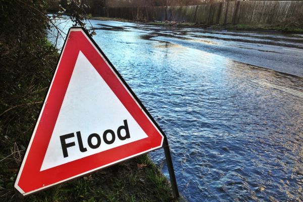Triangle white with red border flooding sign in front of flooded road.