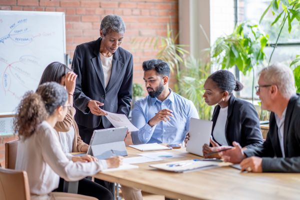Colleagues holding a planning meeting in a conference room. One colleague is standing and showing a report.