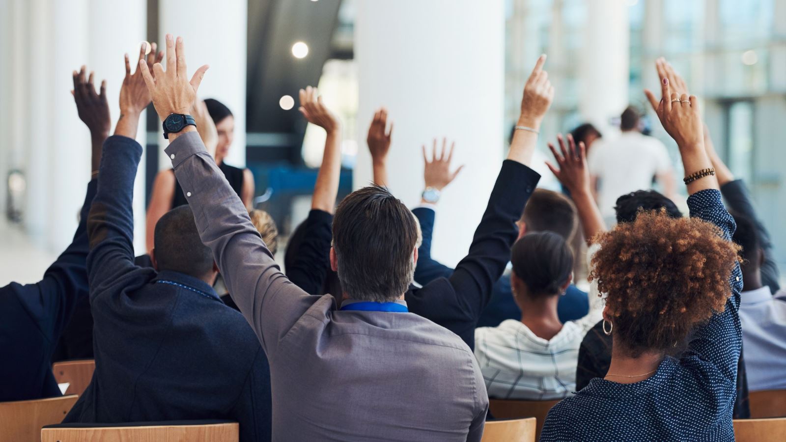 Room filled with people in professional clothing raising hands to ask questions.