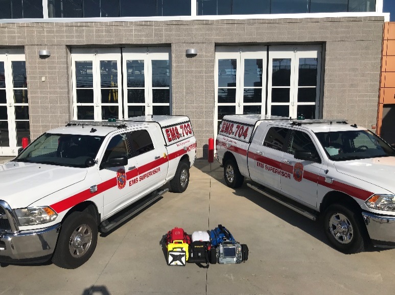 Two EMS trucks and some EMS equipment in front of a fire station
