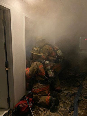 Two fire fighters in the entry way of a smoke filled room