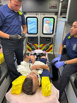 Two EMTs in the back of an ambulance tending to a patient on a cot