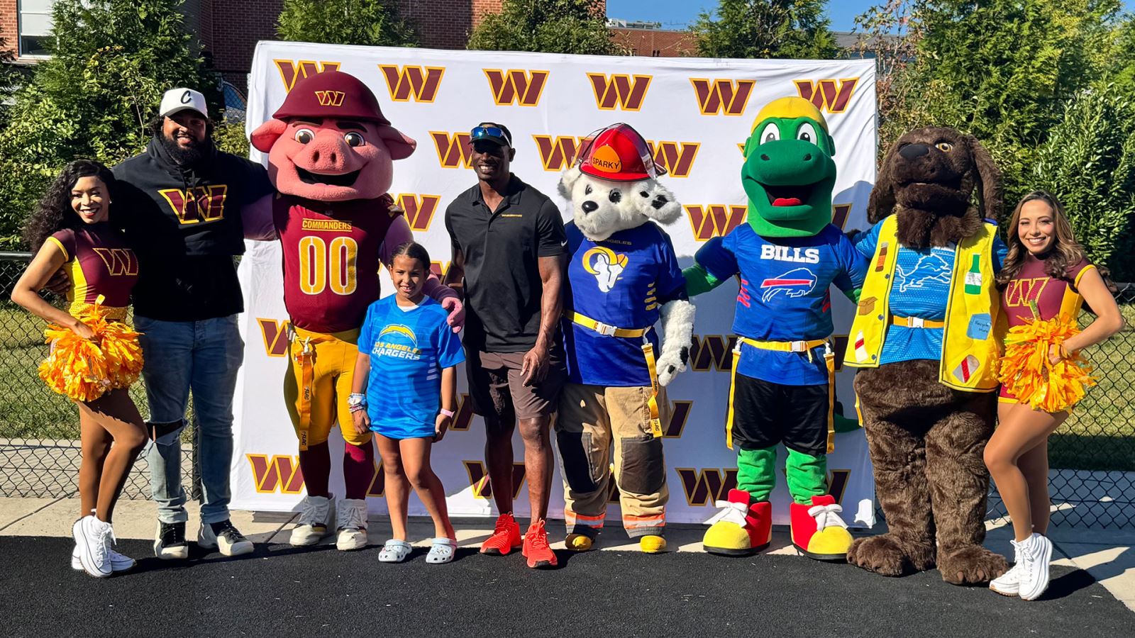 former washington commanders players along with mascots and cheerleaders take photo with youth flag football player